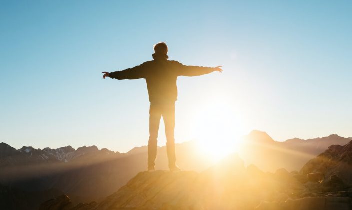 A man standing on top of the hill and welcoming morning sun